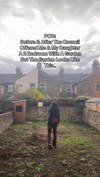 A woman stands in a neglected, muddy garden with sparse vegetation, looking toward a brick house.