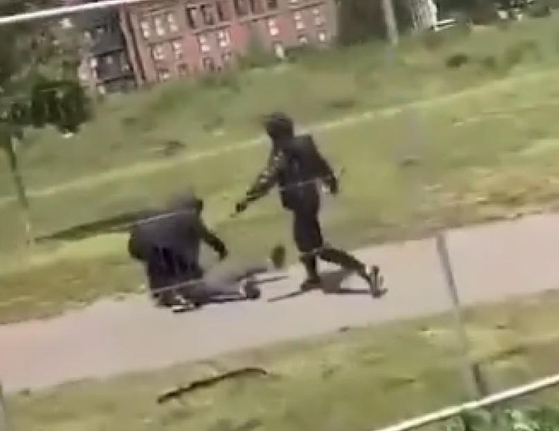 Two people on a pathway in a park, one is crouched over a third person on the ground, while the other stands nearby, and a caption that reads "This is London".