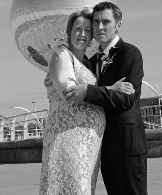 Black and white photo of Sarah Lundy and her late husband Darren embracing in front of a giant disco ball.