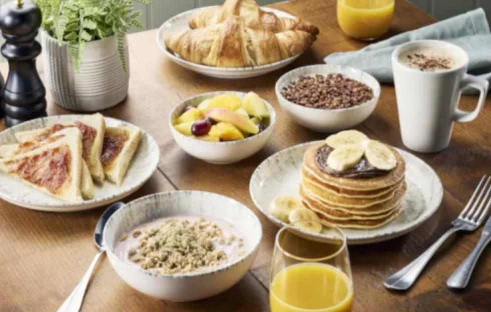 An array of breakfast items including croissants, pancakes, fruit salad, toast with jam, cereal, yogurt, and orange juice.