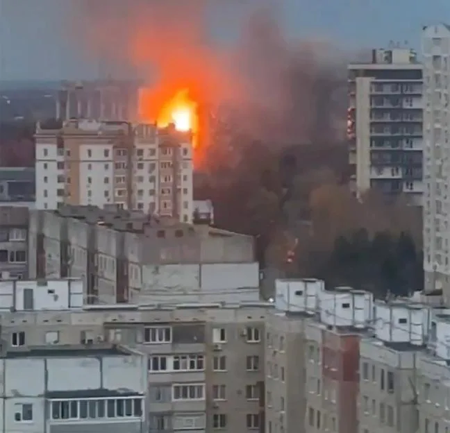 Explosion and thick smoke rising behind apartment buildings, with a missile circled in the sky above.