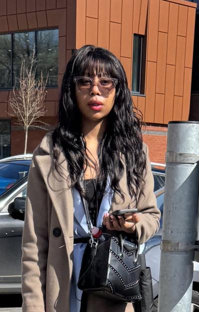 Hadiza Atunse with long dark hair, wearing sunglasses and a beige coat, holding a handbag.