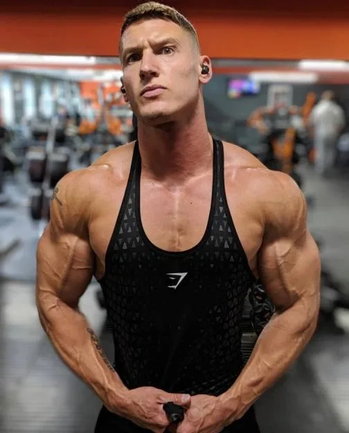 Matt Morsia, also known as Legend from the TV show Gladiators, poses in a gym wearing a black tank top.