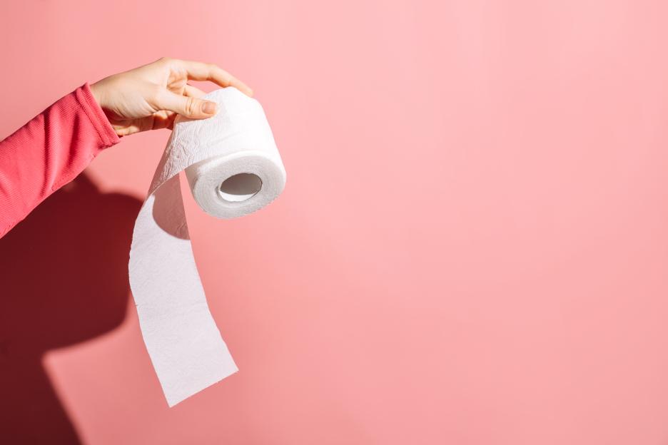 young woman holding toilet paper roll on pink background