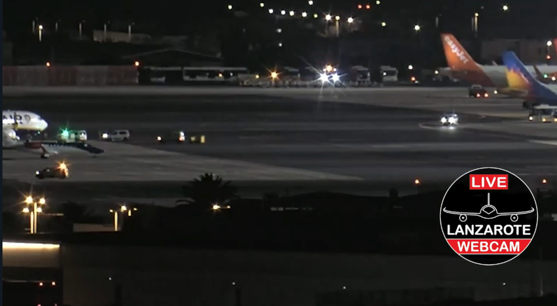 Nighttime photo of an airport tarmac with planes and vehicles, featuring a "Lanzarote Webcam LIVE" overlay.