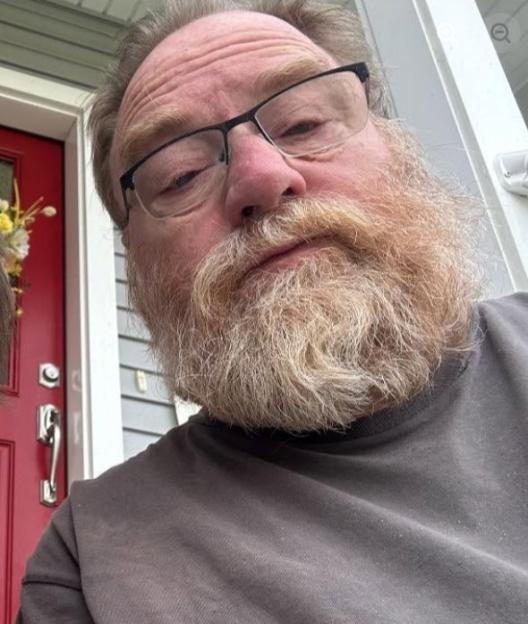 A man with glasses and a beard, in a gray shirt, taking a selfie.