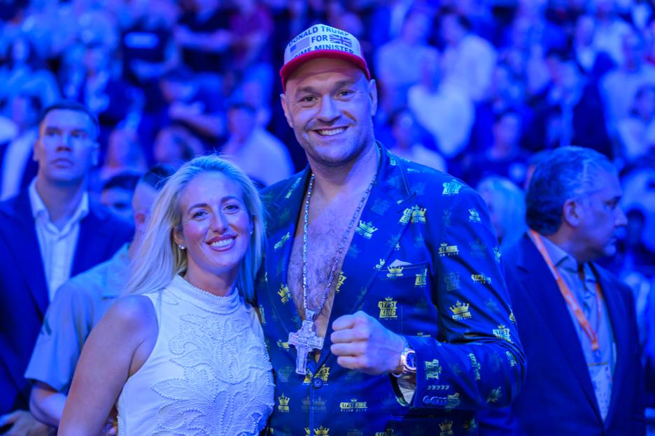 Tyson Fury wearing a red hat that says "Donald Trump for Prime Minister" and a patterned suit, next to a blonde woman.