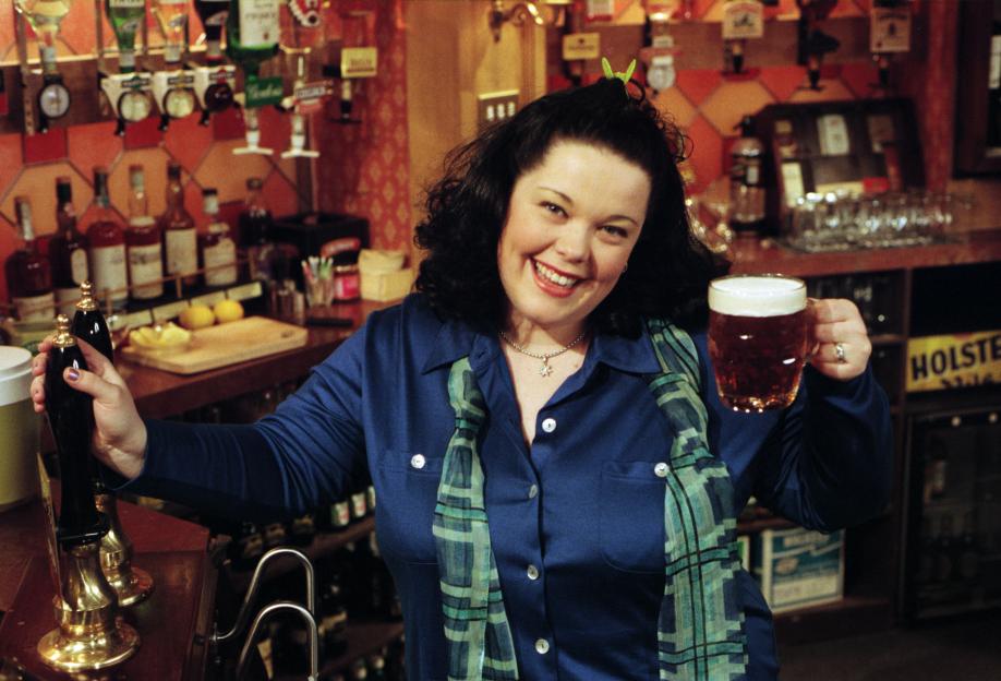 Mandy Dingle, played by Lisa Riley, smiling and holding a pint of beer in a pub.
