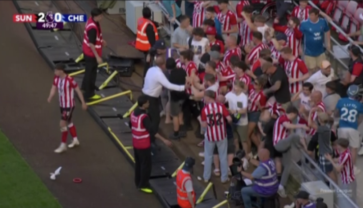Sunderland fans celebrating on the field, wearing red and white striped jerseys, surrounded by security.