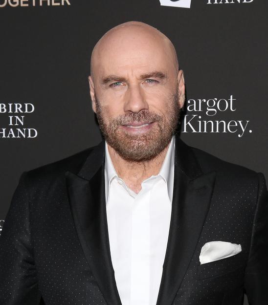 John Travolta in a black suit with a white shirt and pocket square.