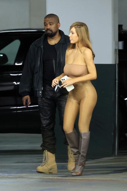 Kanye West and Bianca Censori walking together with Bianca holding a phone and car keys.