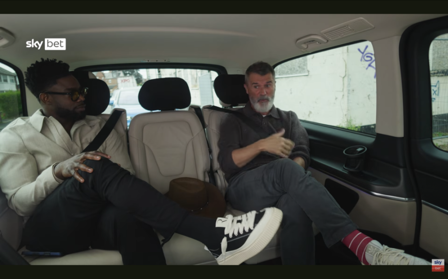Two men sitting in the back of a car, with one man talking and gesturing with his hands.