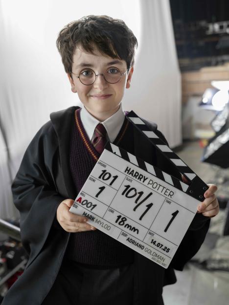 A young boy dressed as Harry Potter holds a clapperboard for a Harry Potter film.