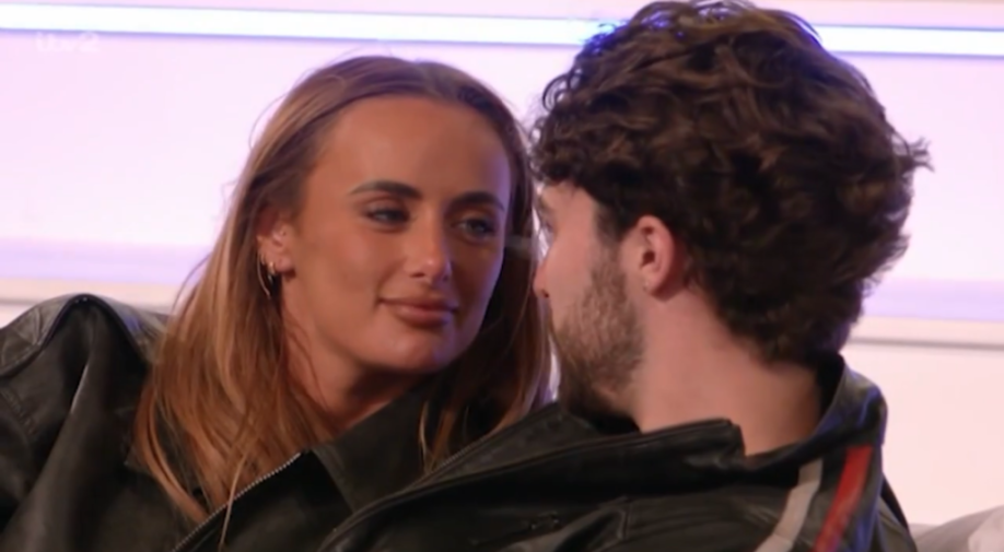 A woman with light brown hair and a man with dark curly hair looking at each other intently.