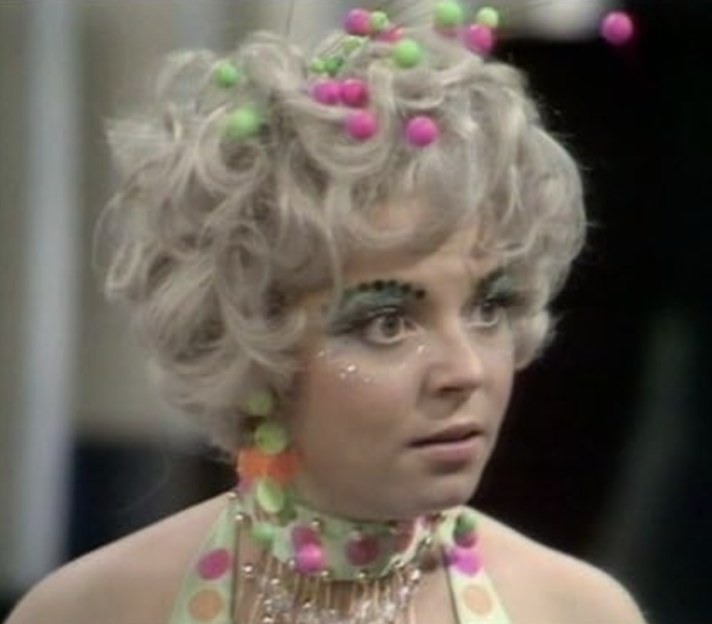 Cheryl Hall in Doctor Who, dressed in costume with sparkly makeup and small, colorful balls in her hair.