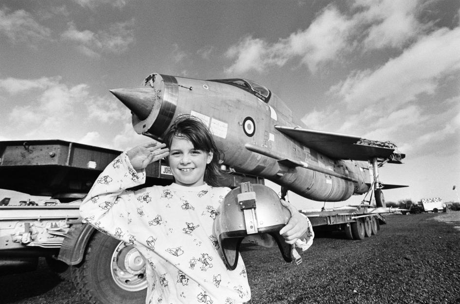 Eight-year-old Cheryl James saluting beside a T55 Lightning fighter jet at the Midland Air Museum.