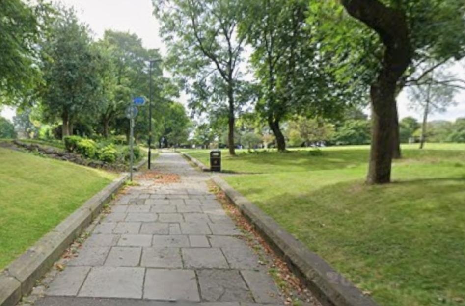 A paved path in Broadfield Park flanked by grass and trees.