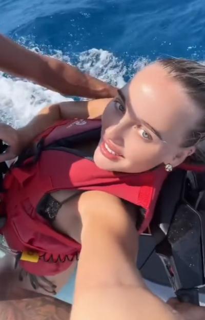 A woman wearing a red life vest poses for a selfie while on a watercraft.