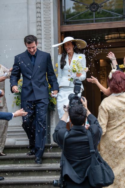 Dua Lipa and Callum Turner exiting a Westminster Registry office, surrounded by falling confetti and photographers.