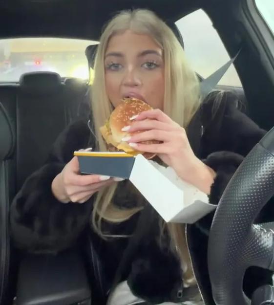 A woman in a car eating a burger from a fast food container.