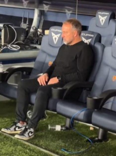 Hansi Flick sits on a bench, looking downcast.