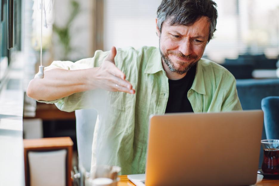 Stressed man waving his hands in front of a laptop at a cafe.