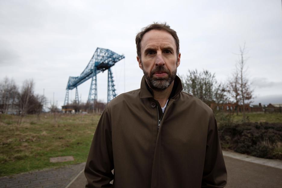 Gareth Southgate standing in front of a blue suspension bridge.