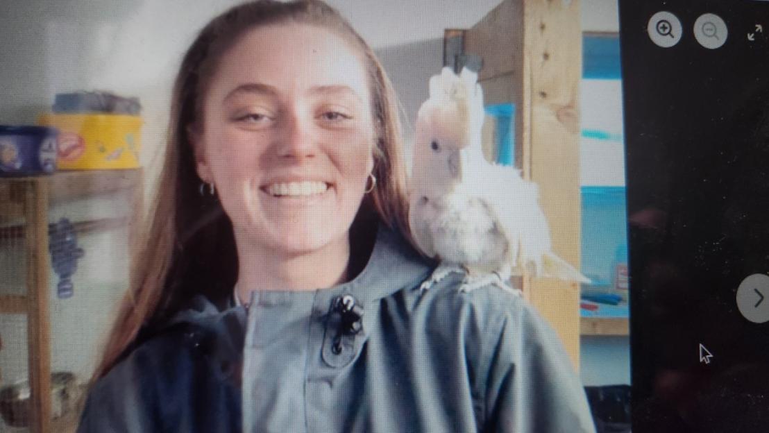 A smiling young woman with a white cockatoo on her shoulder.