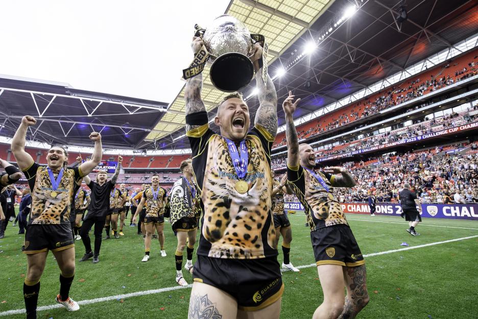 Leigh Leopards players celebrating their Challenge Cup victory, with one player holding the trophy aloft.