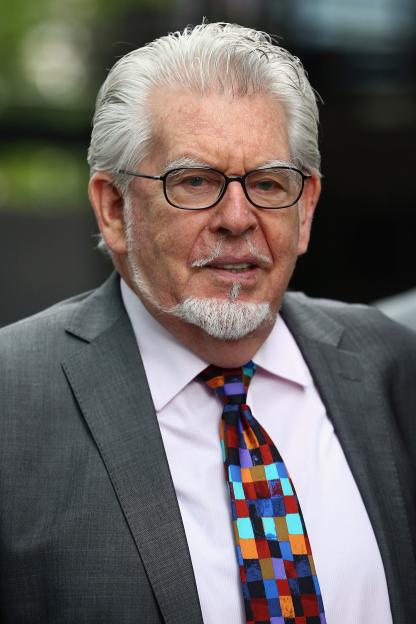 Entertainer Rolf Harris, with gray hair and beard, wearing glasses, a suit, and a colorful tie, arriving at Southwark Crown Court.