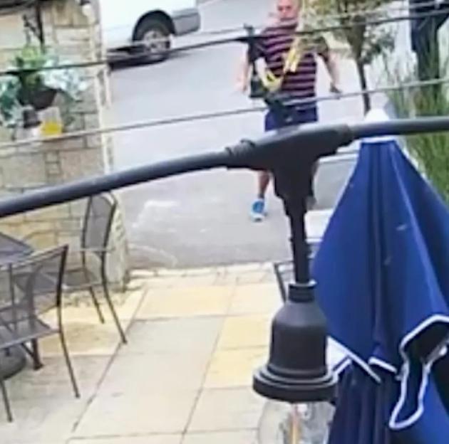 Security camera footage of a man in a striped shirt and shorts stumbling away from a pub.
