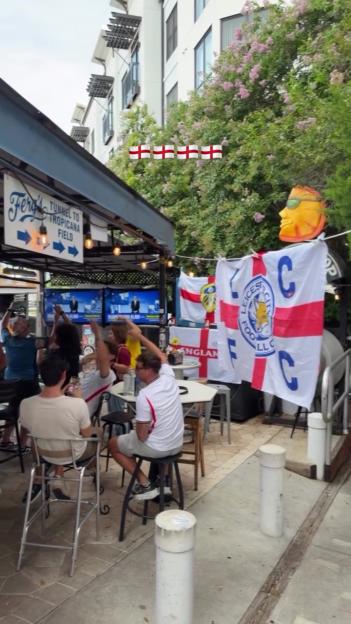 People watching football at an outdoor bar in Florida, decorated with English football flags.