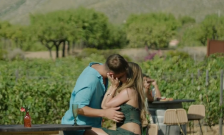 A man and woman kissing outdoors in a vineyard.