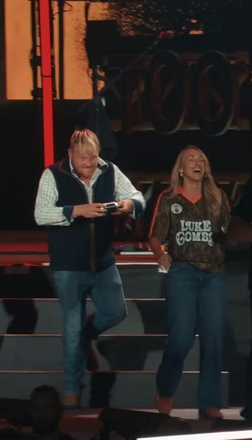 Kaleb Cooper prepares to shotgun a can of lager on stage next to a laughing woman in a "Luke Combs" shirt.