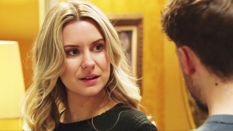 A woman with blonde hair looking towards a man's back, facing him.