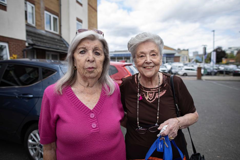 Elsie Humphries and Annie Secunda standing on a street in front of parked cars.