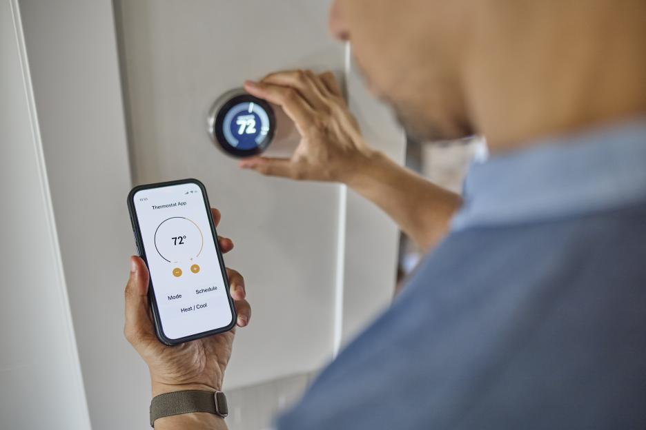 Man using a smartphone app to control a smart thermostat.