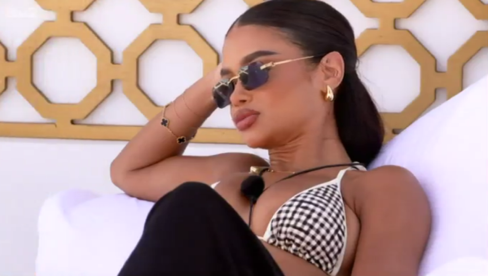 A woman in sunglasses and a black and white checkered bikini top reclining on a white pillow.