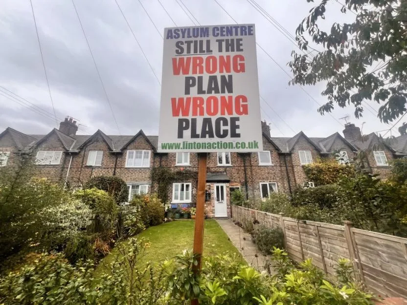 A protest sign reading "Asylum centre still the wrong plan wrong place" in front of terrace houses in Linton-on-Ouse.