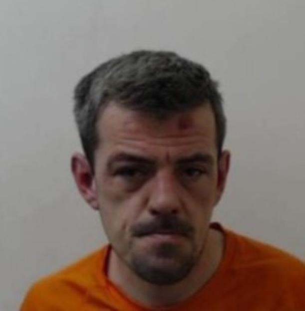 A man with short grey hair, a mustache, and a goatee, wearing an orange shirt.