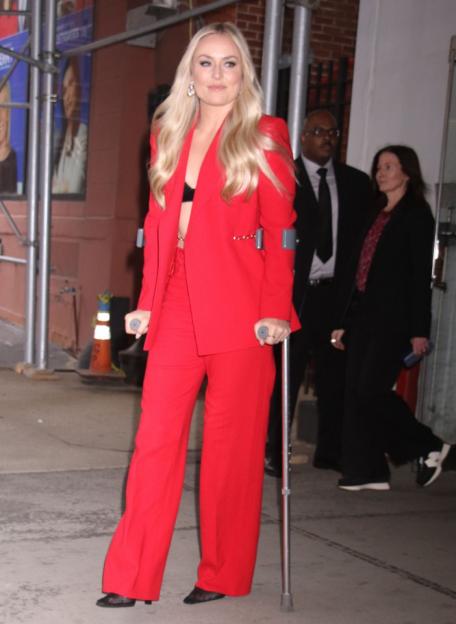 Lindsey Vonn in a red pantsuit and black bralette, using crutches.