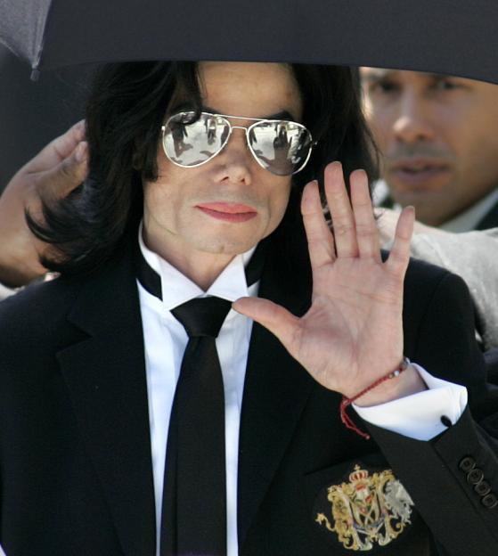 Singer Michael Jackson wearing sunglasses and a black suit leaves the courthouse, waving his hand.