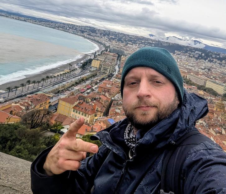 Aleksander Sikora taking a selfie with the city of Nice and the coastline in the background.