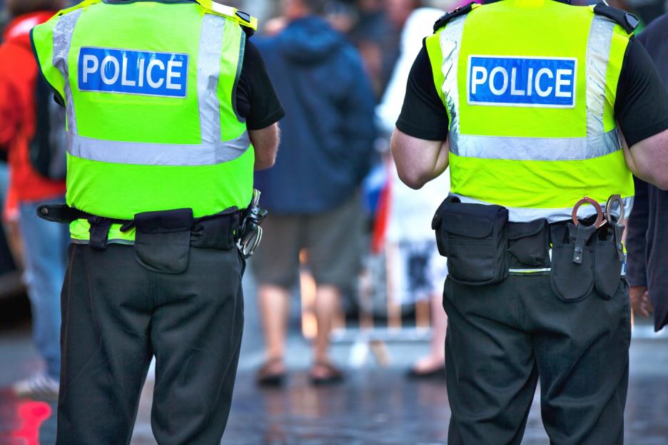 Two police officers from behind wearing neon vests that say "POLICE."