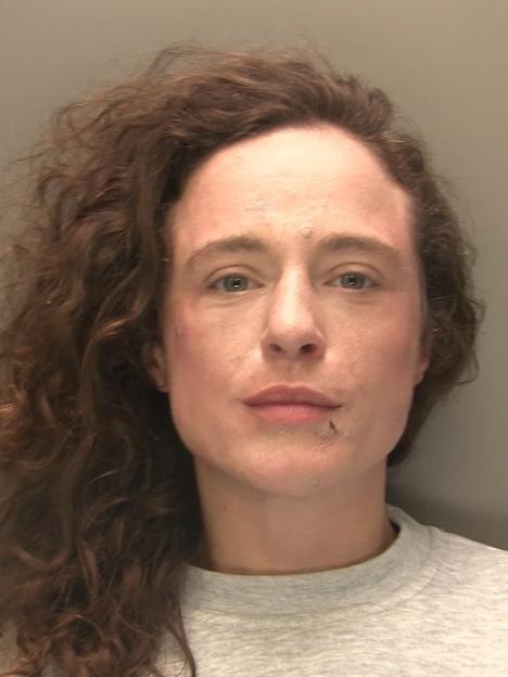 Headshot of Courtney Balloch, a woman with long, curly brown hair and a neutral expression, wearing a gray sweatshirt.