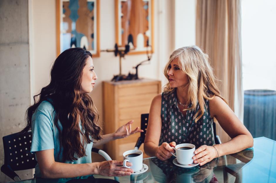 Mother and daughter discussing over coffee at home.