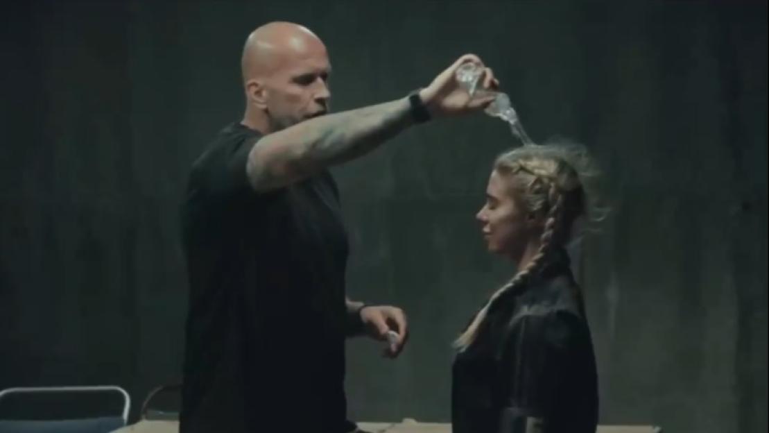 A bald man pouring water over a woman's head.