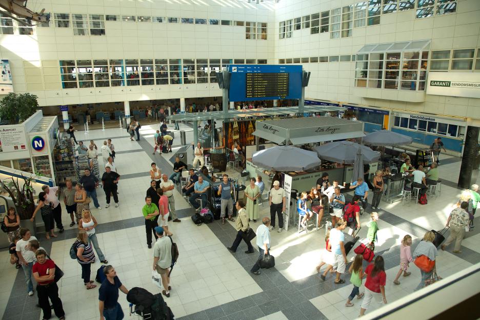 An overhead view of the main hall of the Terminal Building at Bergen Airport Flesland in Norway, with many people standing, walking, or sitting at cafe tables.