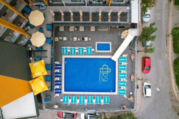 Aerial view of a hotel complex featuring two swimming pools, lounge chairs, dining tables, and shaded areas.