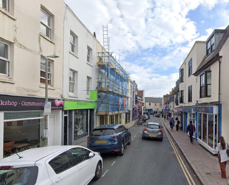 A street lined with buildings, some with scaffolding, and cars parked or driving.